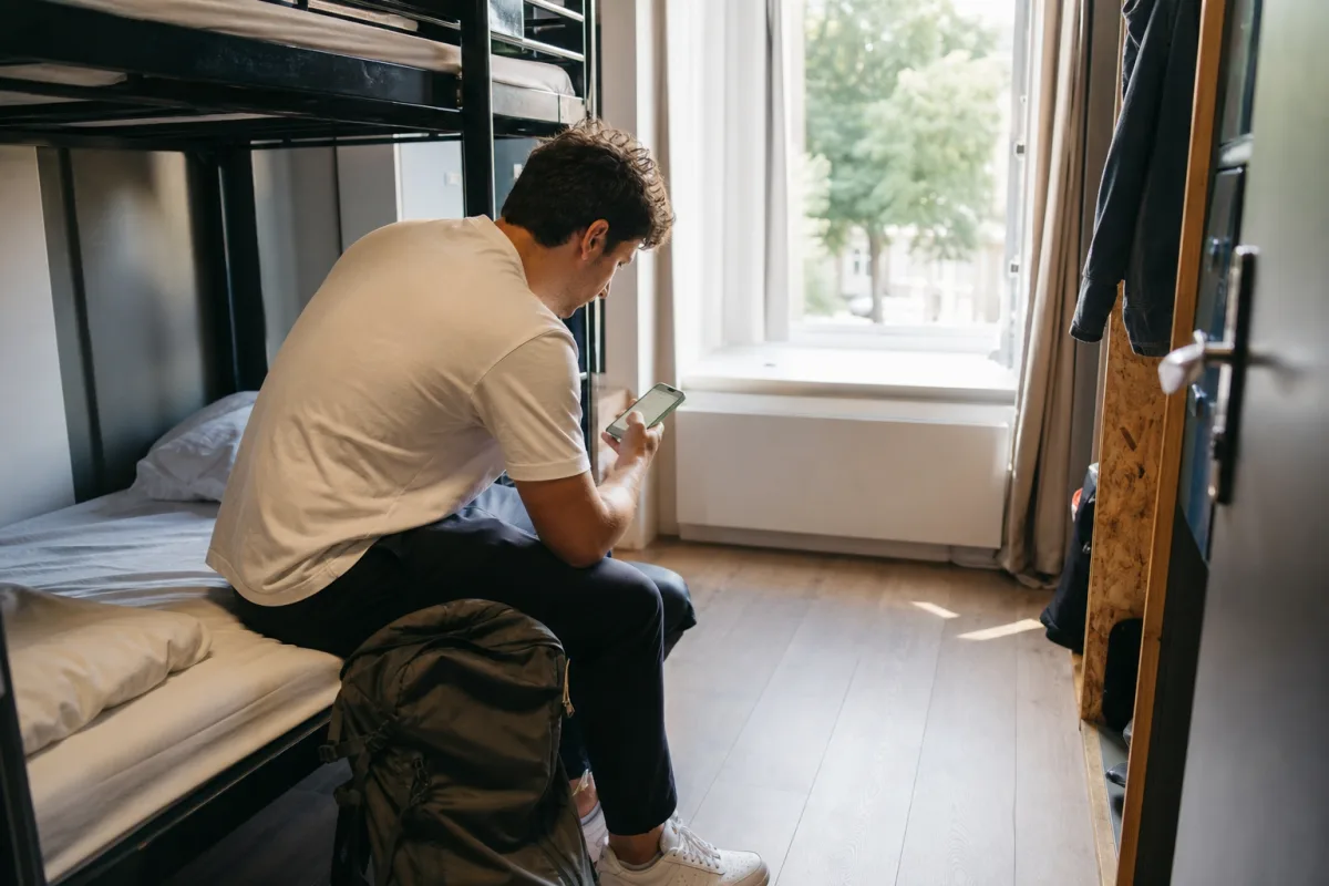 Resenär bokar hostel i mobilen med ryggsäck bredvid